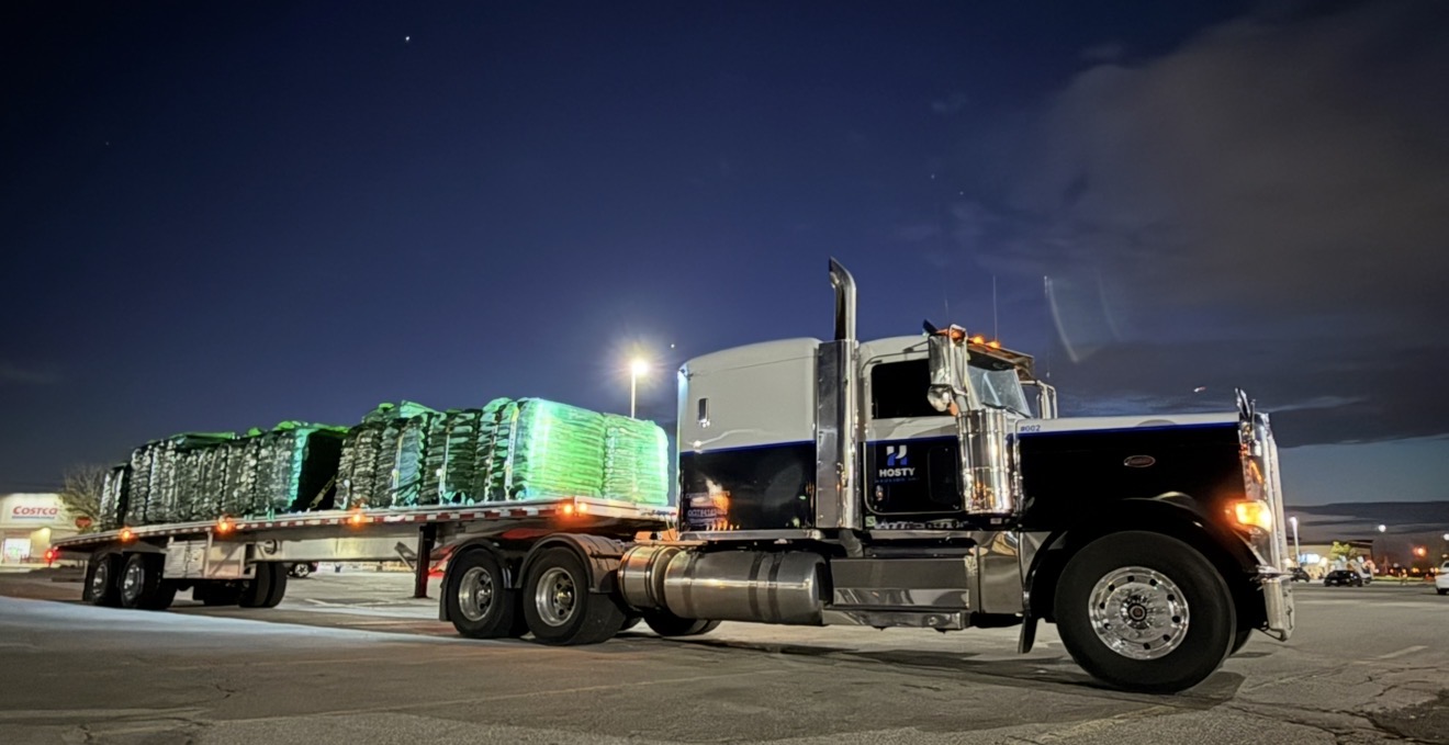 Peterbilt semi truck with a loaded flatbed trailer parked at night with running lights on. 
