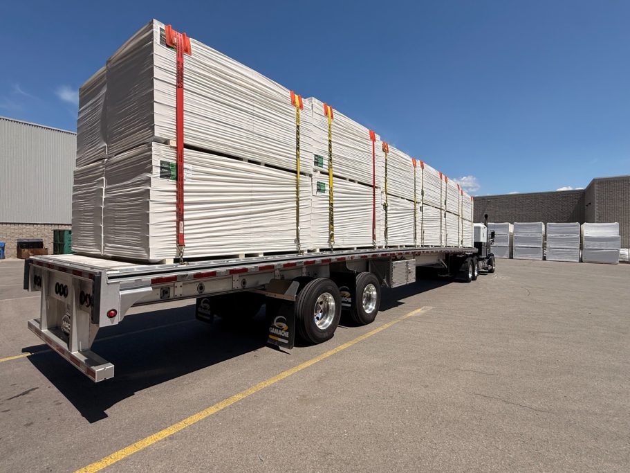 Wrapped insulation panels and building materials secured with straps on a commercial flatbed trailer.
