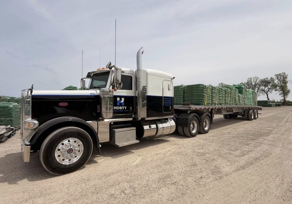 Peterbilt semi truck pulling a flatbed trailer with a securely strapped cargo load in Ontario.
